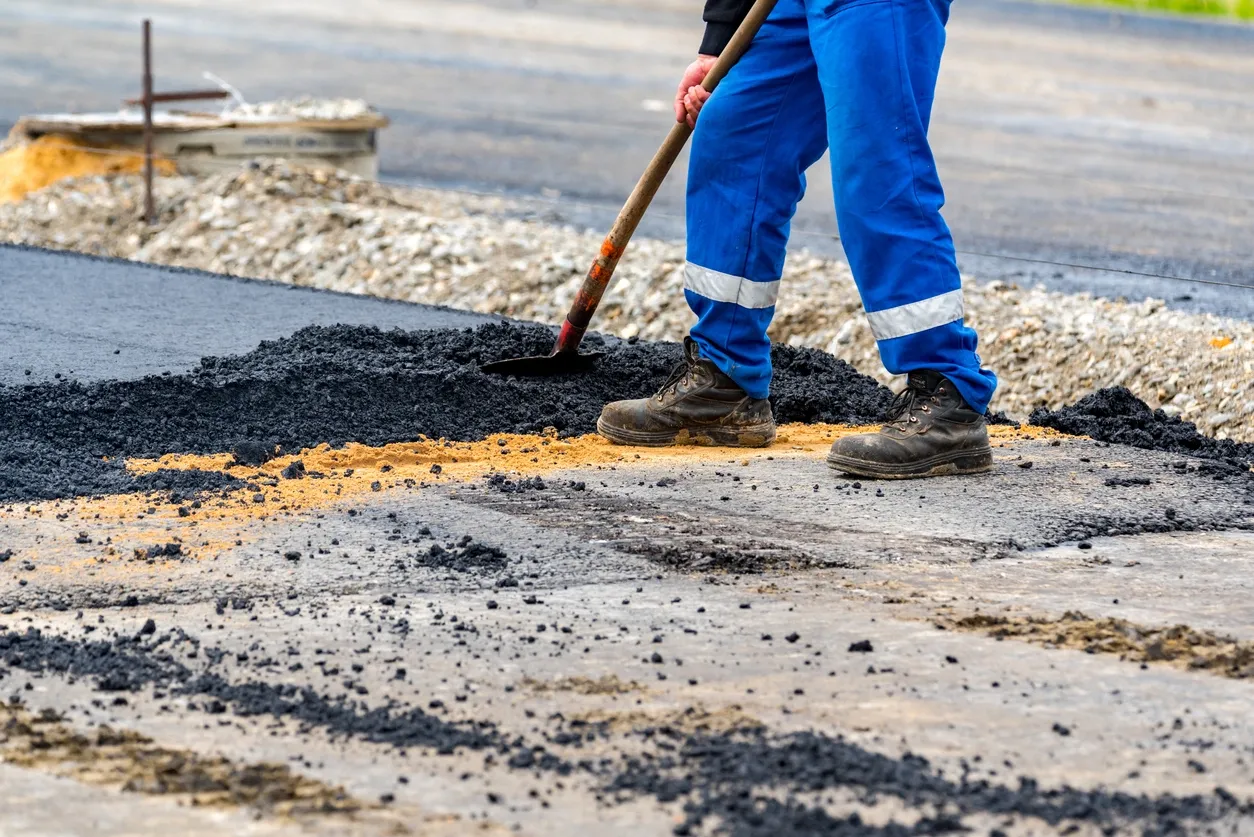 Worker spreading asphalt on road surface.