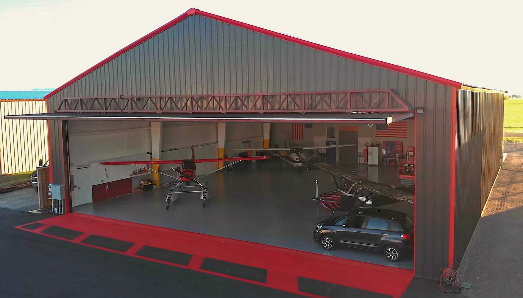 Aircraft and vehicle inside an open hangar.