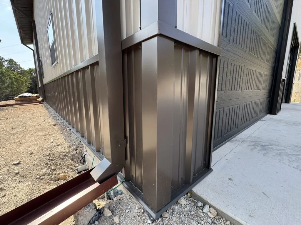 Metal building corner with downspout and garage.