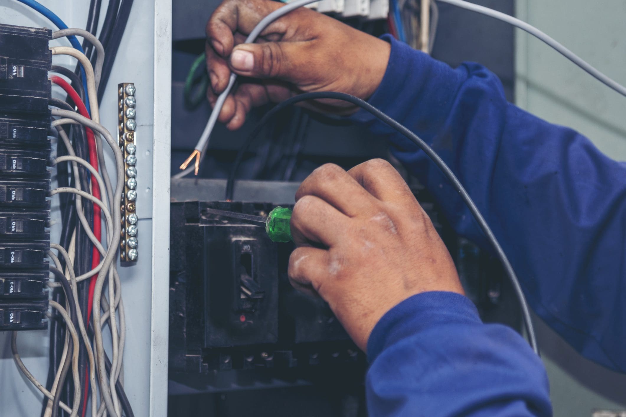Hands working on electrical wiring panel.