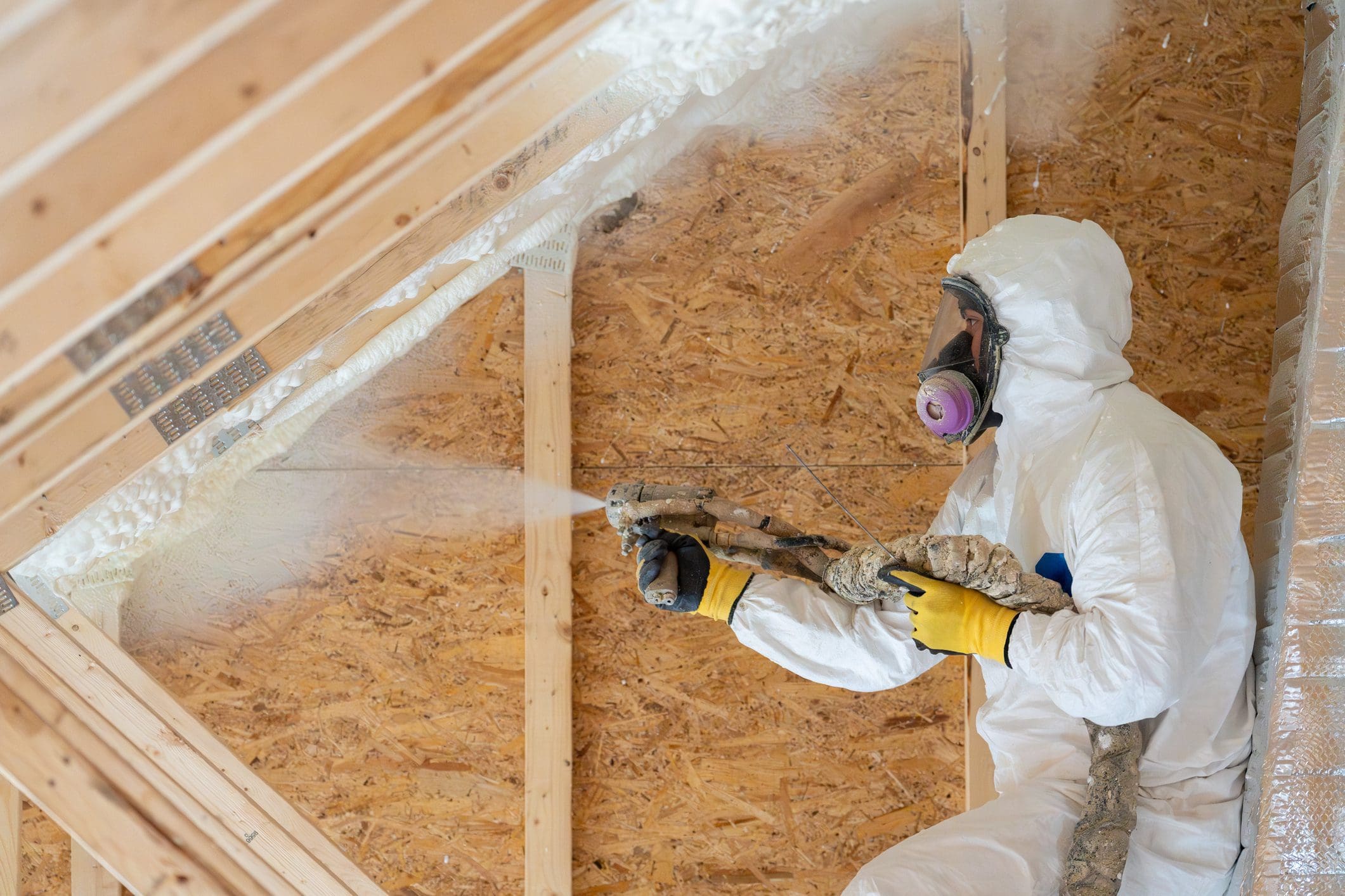 Worker spraying insulation in attic space.