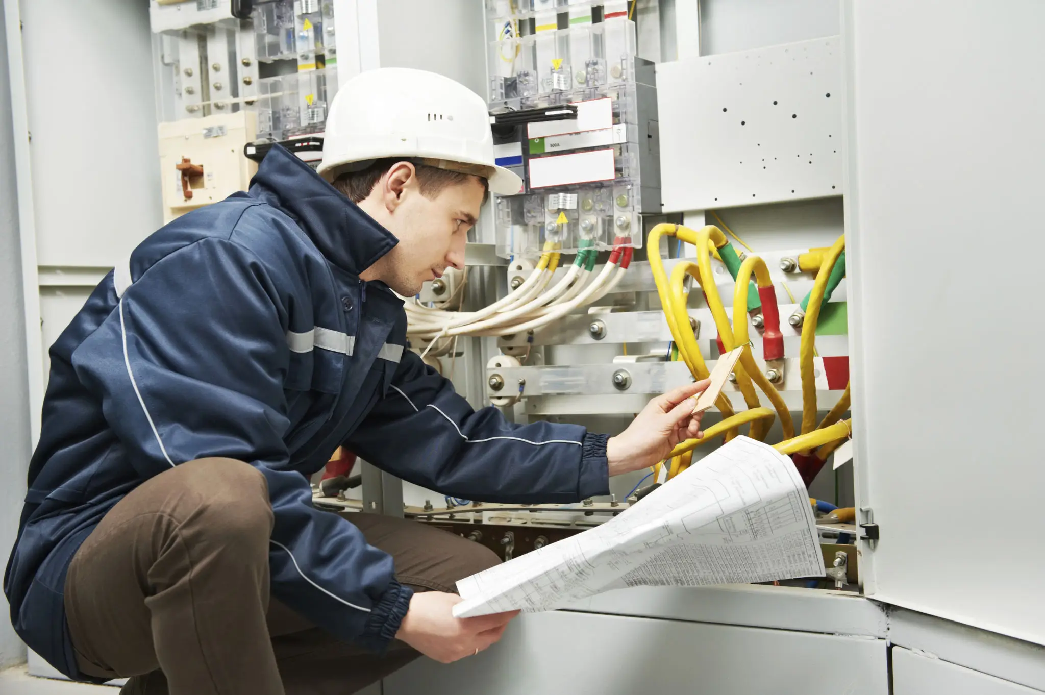 Electrician inspecting electrical panel with documents.