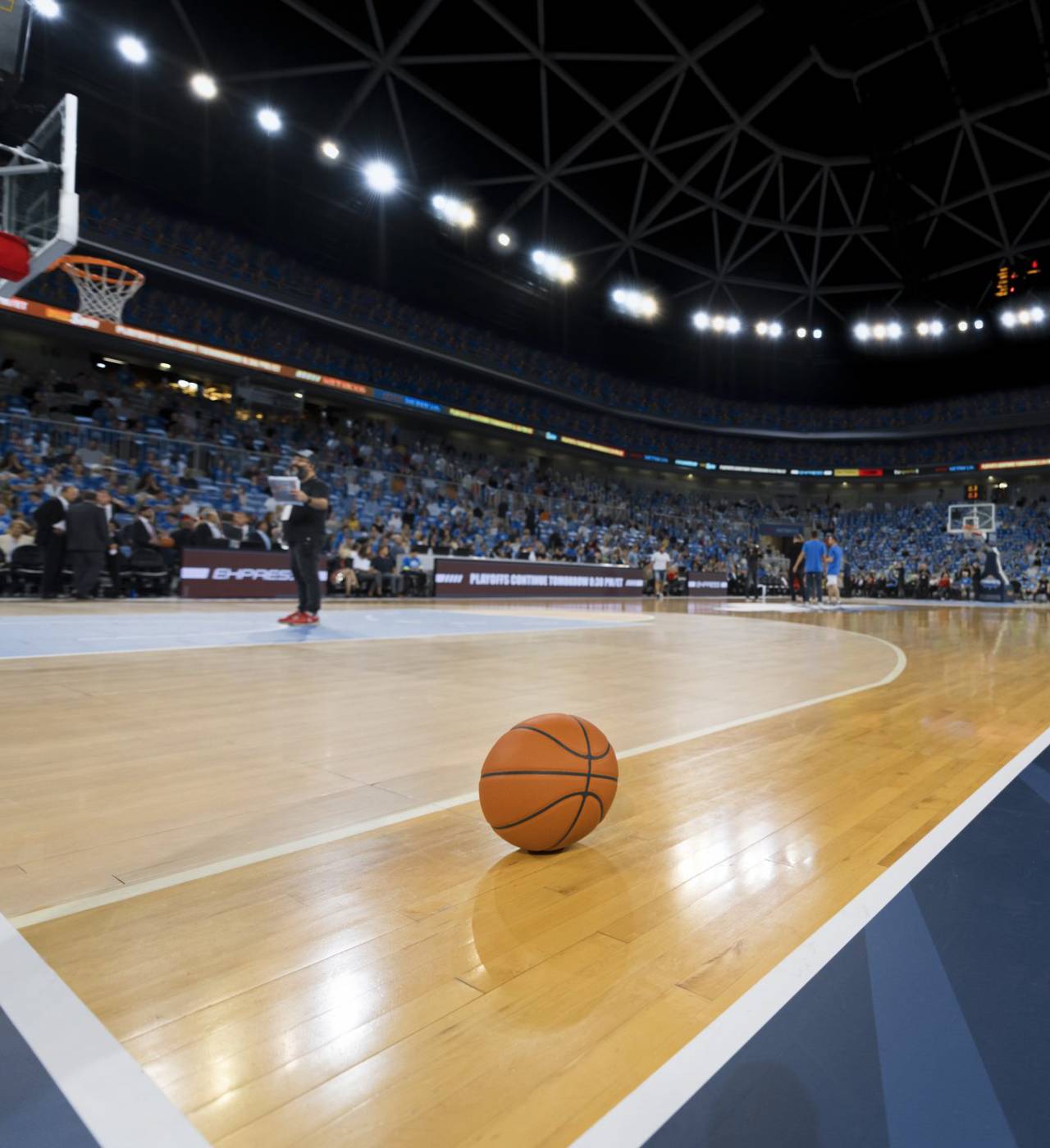 Basketball on court under arena lights.