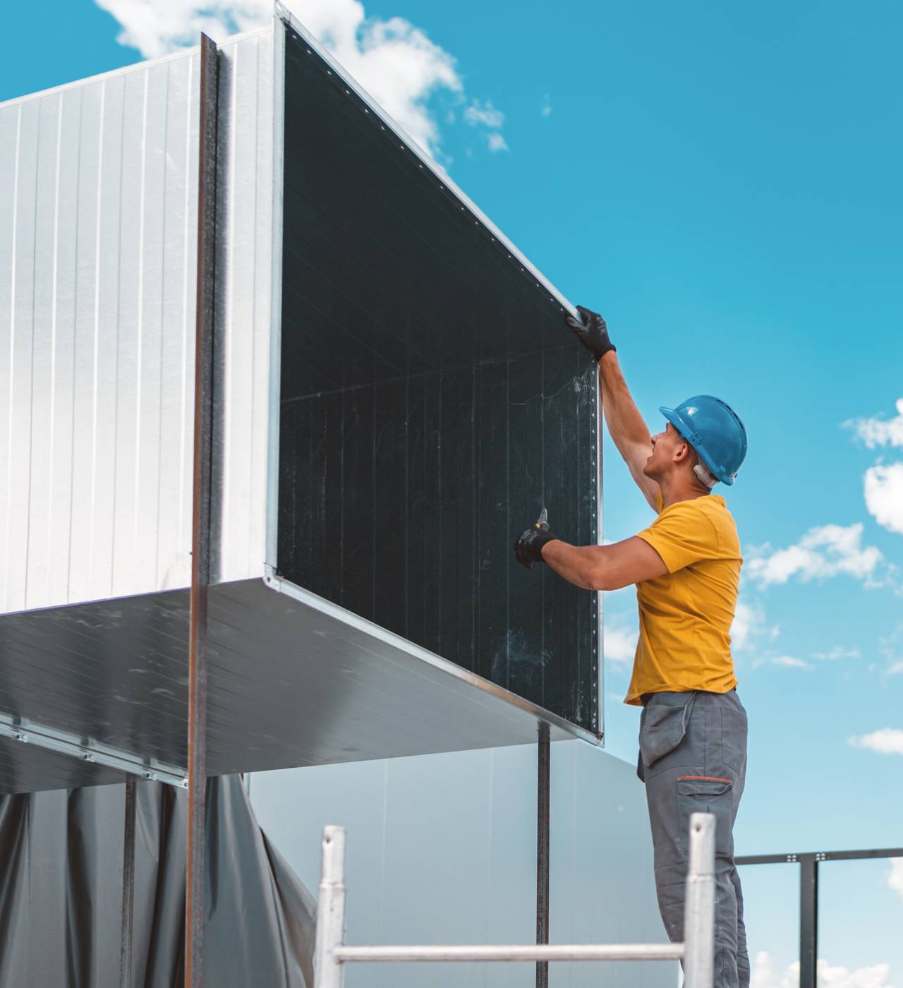 Worker installing metal panel on building.