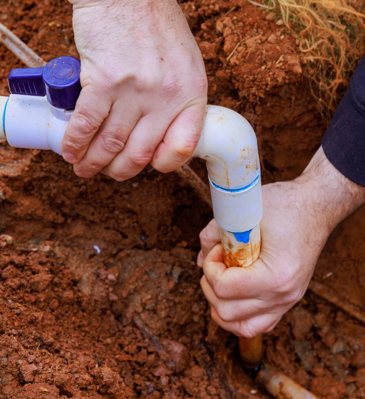 Hands repairing underground PVC water pipe.