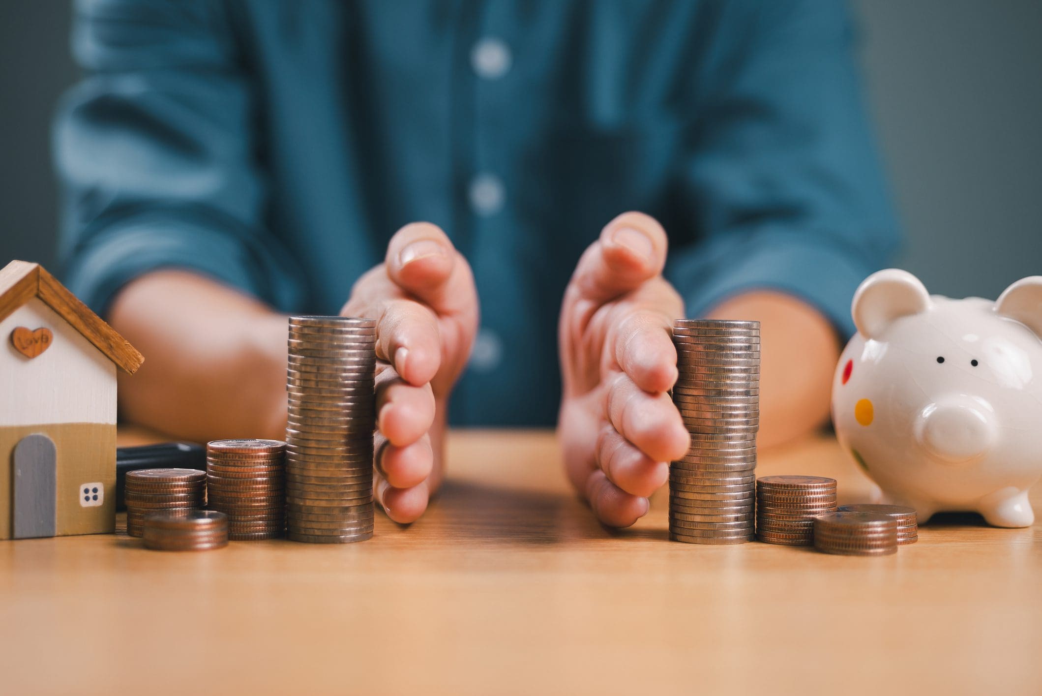 Hands separating coins, house, and piggy bank.