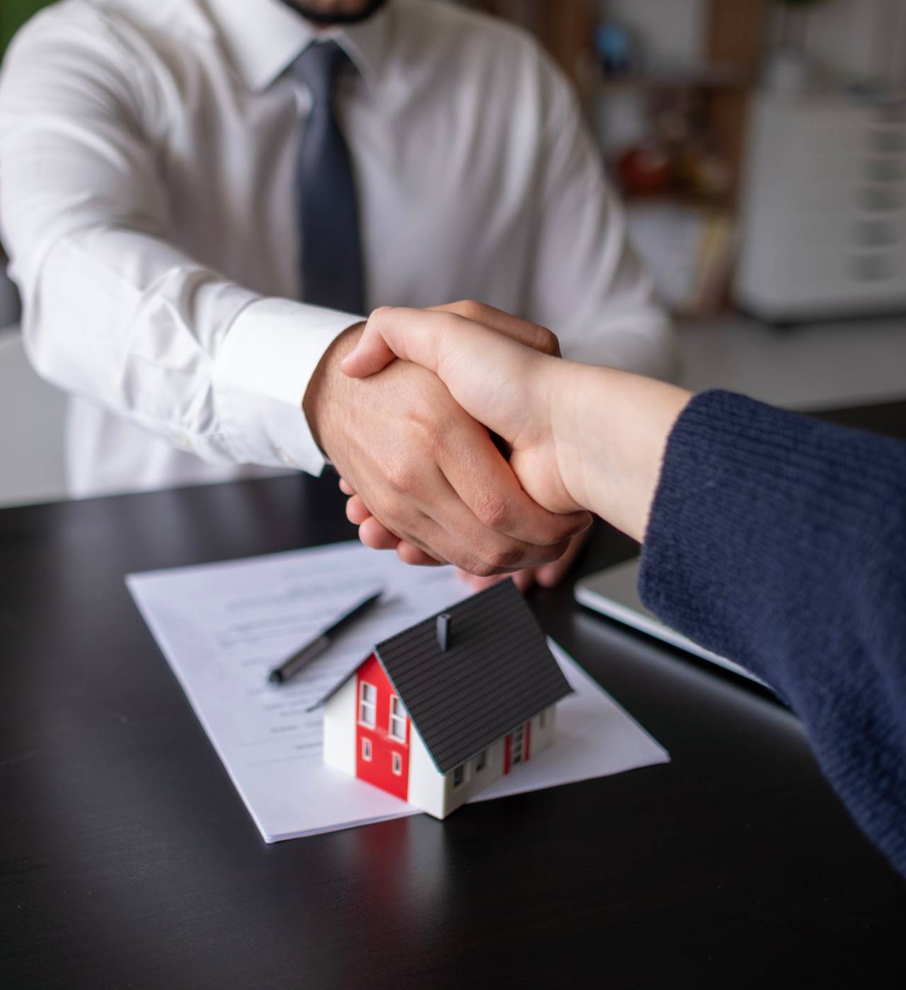 Handshake over real estate contract and model house.