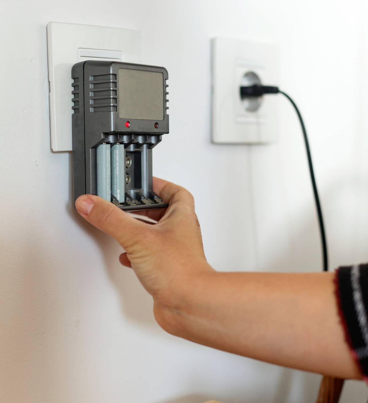 Hand placing battery charger in wall socket.