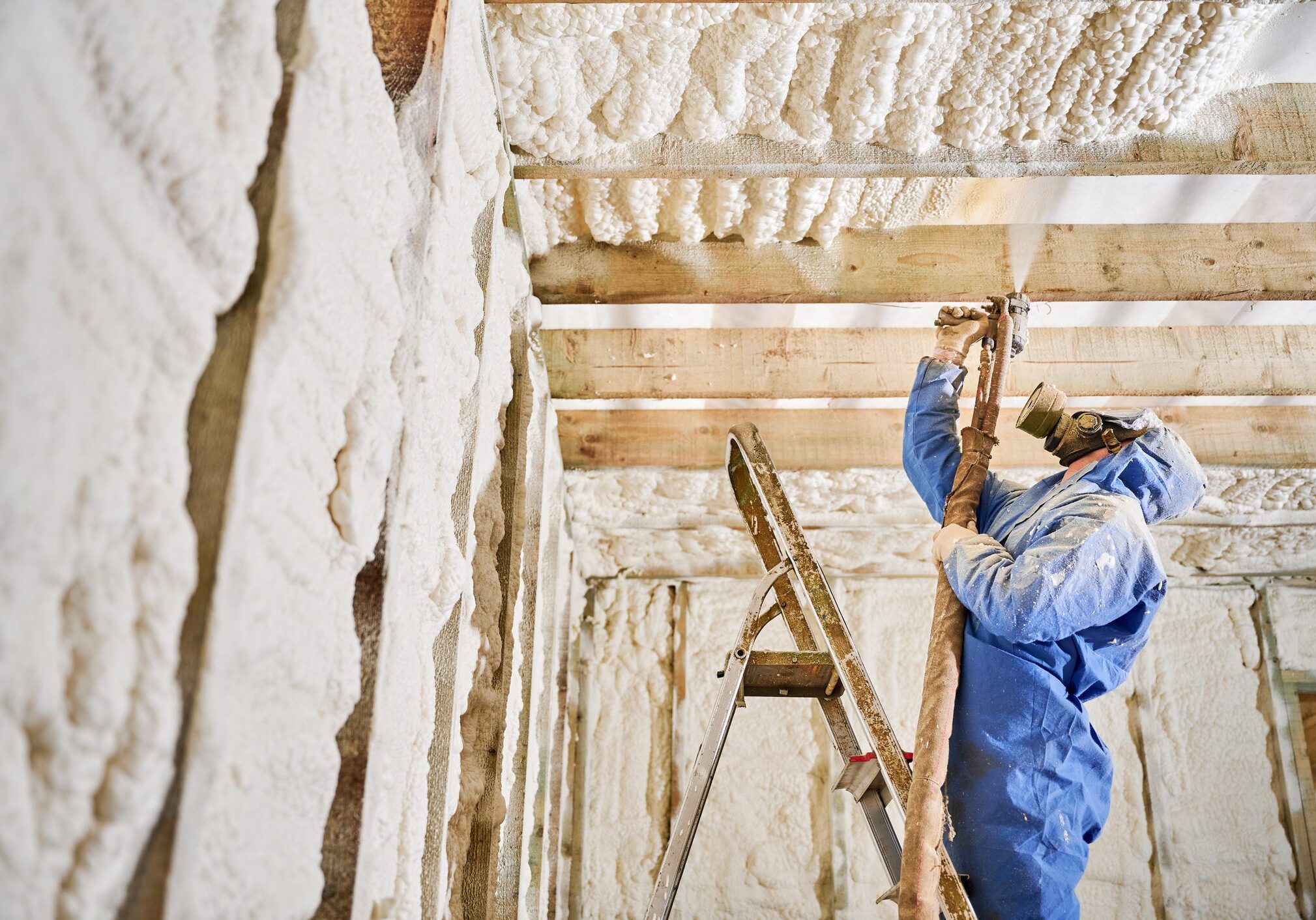 Worker applying spray foam insulation indoors.