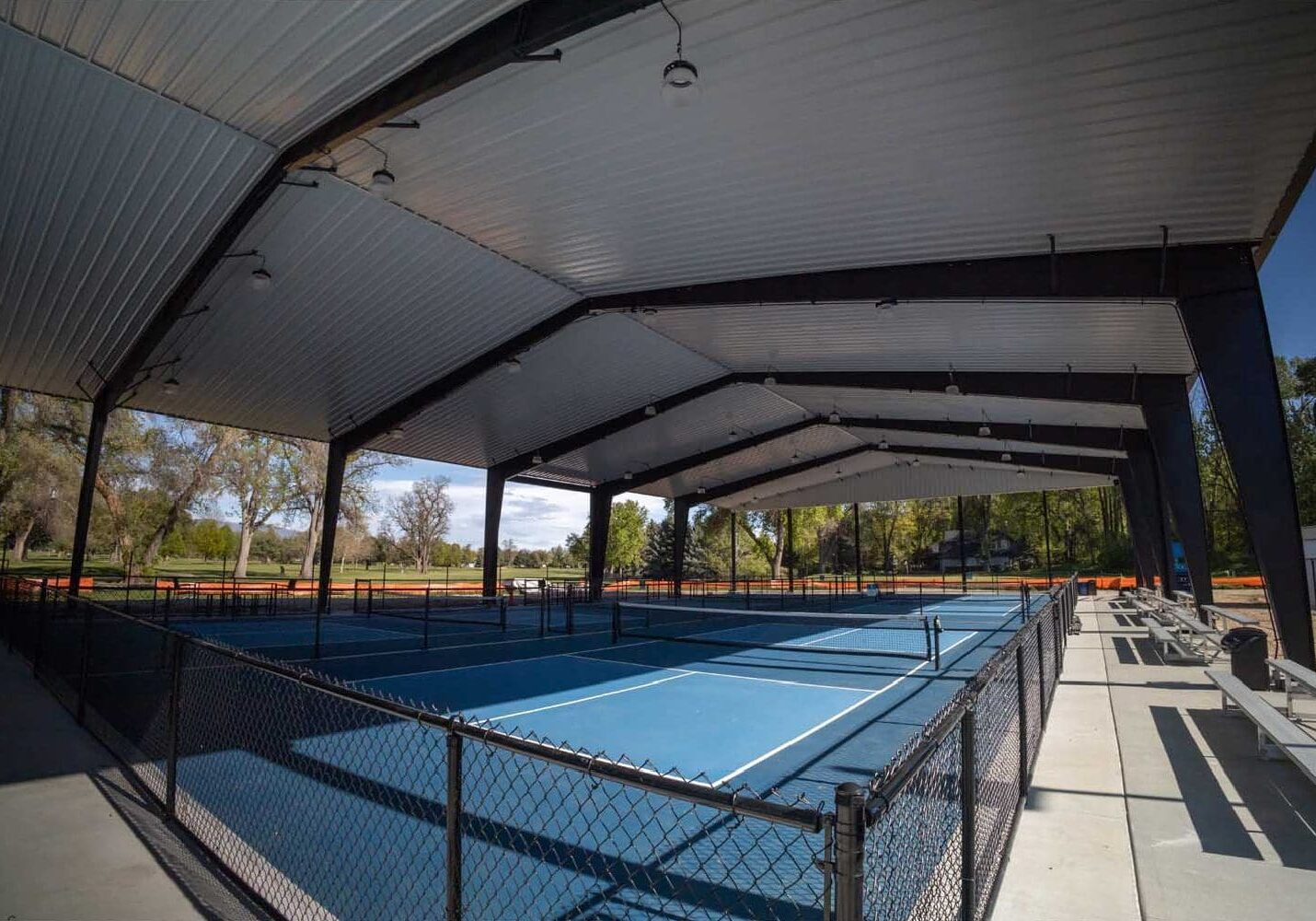 Covered outdoor tennis courts with blue surface.